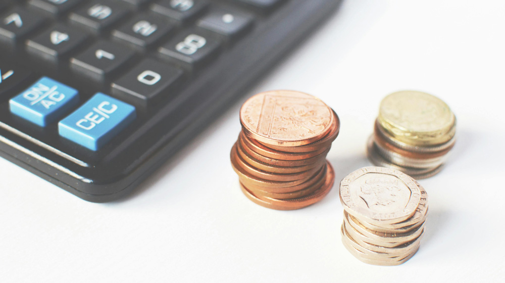 A calculator and a stacked pile of pennies, pence and pounds.