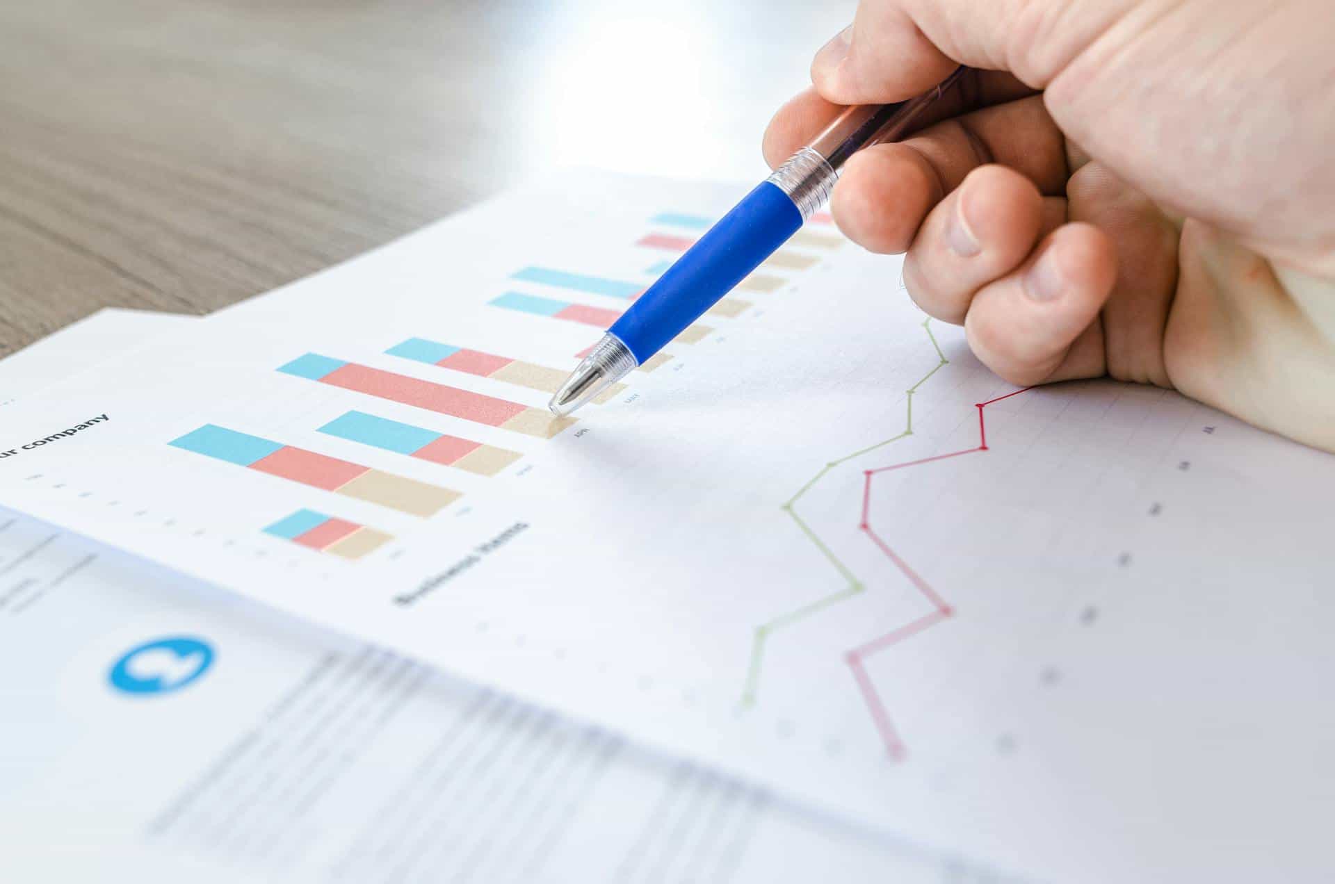 A hand holds a pen while analysing a report.